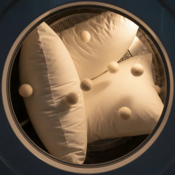 Two white bed pillows tumbling in a dryer with dryer balls to restore fluffiness and ensure even drying.